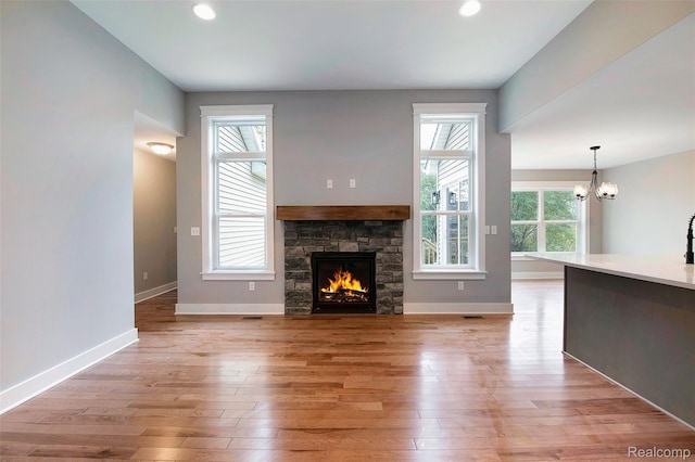 13339 Whispering Pines Ct, Linden, MI 48451 - unfurnished living room featuring a chandelier, light wood-style flooring, a stone fireplace, and recessed lighting