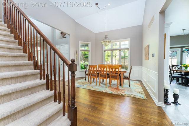 10827 Sparkling Waters Ct, South Lyon, MI 48178 - dining room with stairs, wood finished floors, a chandelier, high vaulted ceiling, and a wainscoted wall