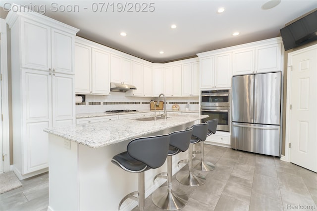 10827 Sparkling Waters Ct, South Lyon, MI 48178 - kitchen featuring stainless steel appliances, decorative backsplash, white cabinets, a center island with sink, and light stone countertops