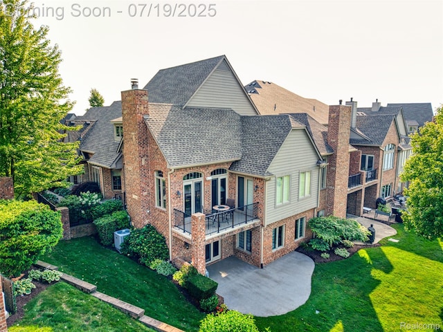10827 Sparkling Waters Ct, South Lyon, MI 48178 - back of property featuring a patio area, a shingled roof, brick siding, a yard, and a balcony
