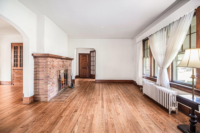 2551 Elmwood Ave, Ann Arbor, MI 48104 - unfurnished living room with radiator, wood finished floors, and a brick fireplace
