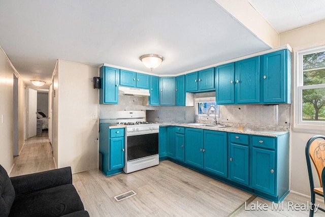 kitchen with blue cabinets, white gas range, light countertops, light wood-type flooring, and decorative backsplash