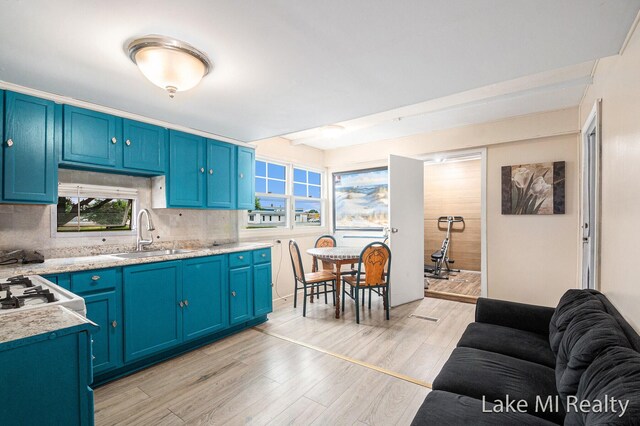 kitchen with light countertops, blue cabinets, light wood finished floors, and decorative backsplash