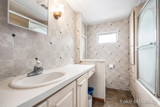 full bath featuring tile walls, vanity, a shower with door, and backsplash