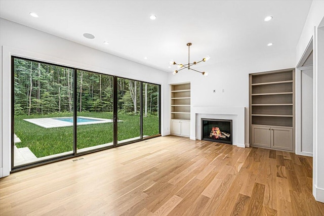 7462 Youngren Rd, Three Oaks, MI 49128 - unfurnished living room with built in features, a chandelier, light wood-style flooring, recessed lighting, and a lit fireplace