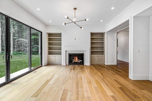 7462 Youngren Rd, Three Oaks, MI 49128 - unfurnished living room with built in features, wood finished floors, a chandelier, recessed lighting, and a lit fireplace