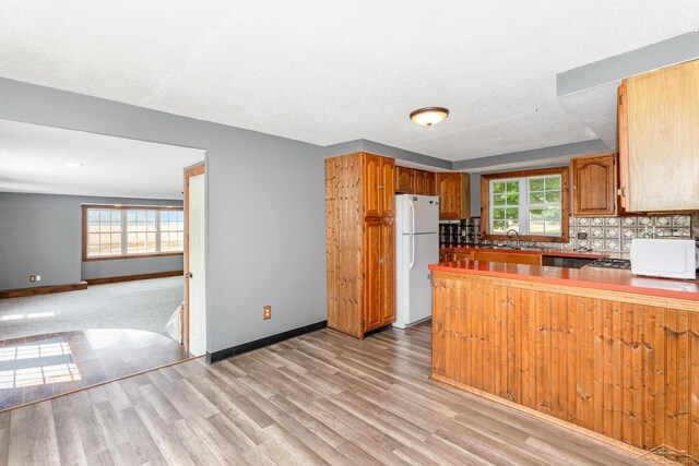 5010 N Pendell Rd, Alma, MI 48801 - kitchen featuring light wood-style floors, white appliances, a peninsula, and brown cabinetry