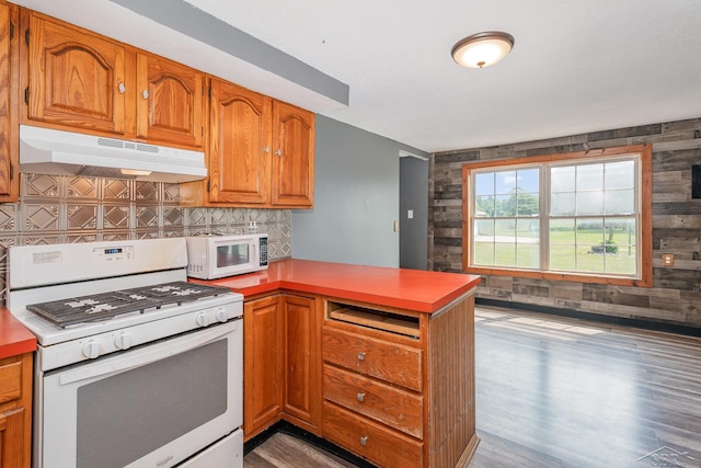 5010 N Pendell Rd, Alma, MI 48801 - kitchen with white appliances, a peninsula, under cabinet range hood, wood finished floors, and decorative backsplash
