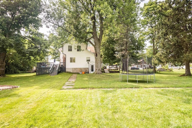 1193 Seneca St, Adrian, MI 49221 - view of grassy yard featuring a trampoline, a wooden deck, and stairway