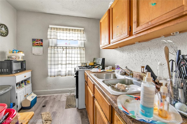 13528 Ardmore St, Detroit, MI 48227 - kitchen featuring wood finished floors, a textured wall, gas stove, black microwave, and brown cabinets