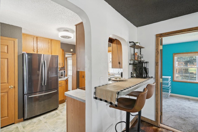 1903 Bucholtz Hwy, Deerfield, MI 49238 - kitchen featuring arched walkways, freestanding refrigerator, a textured ceiling, light countertops, and a kitchen bar