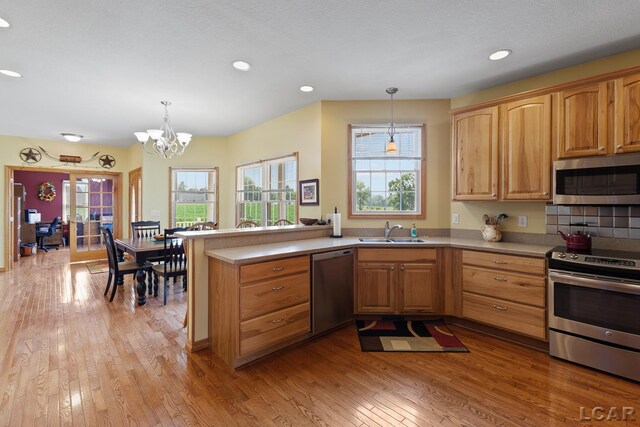 5726 Wolf Creek Hwy, Adrian, MI 49221 - kitchen featuring appliances with stainless steel finishes, a peninsula, a chandelier, light wood-style flooring, and plenty of natural light