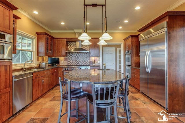 kitchen featuring wall chimney range hood, sink, stainless steel appliances, and decorative light fixtures