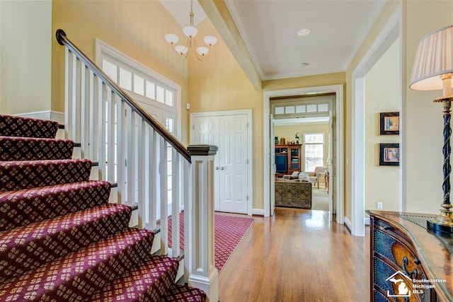 foyer entrance featuring a chandelier, ornamental molding, a towering ceiling, and light hardwood / wood-style flooring