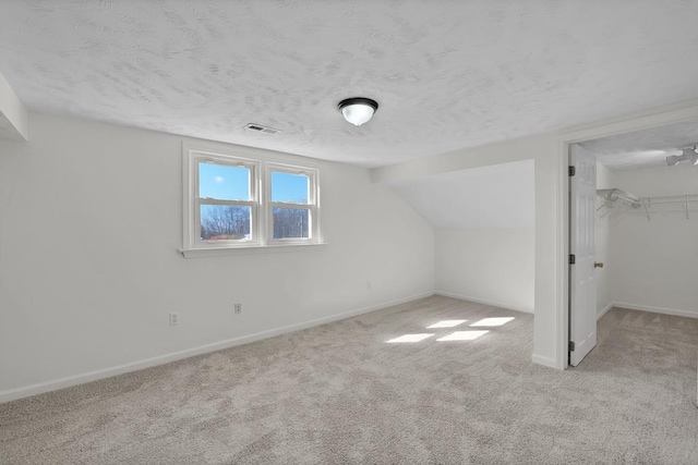 bonus room featuring vaulted ceiling, light colored carpet, and a textured ceiling