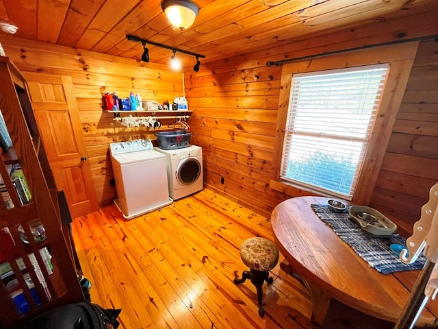 clothes washing area with washer and dryer, wood walls, rail lighting, wooden ceiling, and light wood-type flooring