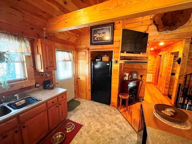 kitchen with lofted ceiling, sink, black fridge, wooden ceiling, and wooden walls