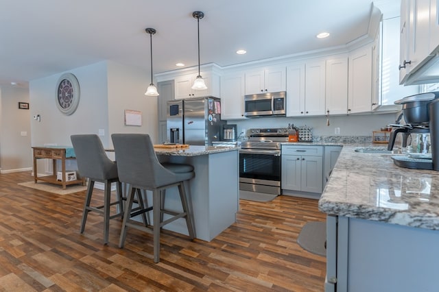 kitchen with decorative light fixtures, white cabinetry, a center island, stainless steel appliances, and light stone countertops