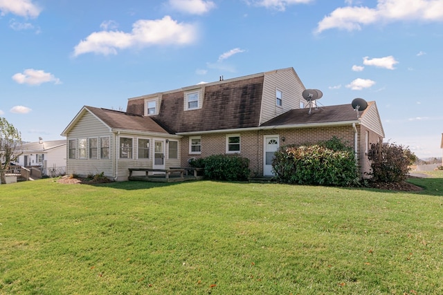 back of property with brick siding, roof with shingles, a gambrel roof, and a yard