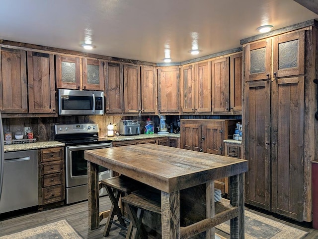 kitchen with stainless steel appliances, light wood-type flooring, backsplash, and glass insert cabinets