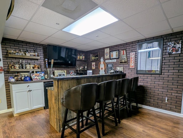 bar with a paneled ceiling, indoor wet bar, and wood finished floors