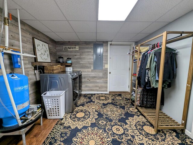 finished basement featuring electric panel, baseboards, a paneled ceiling, wood walls, and separate washer and dryer