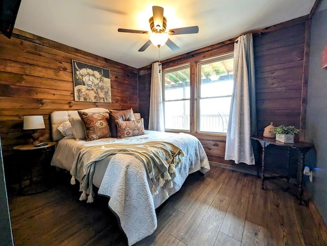 bedroom with ceiling fan, wooden walls, and dark wood-type flooring