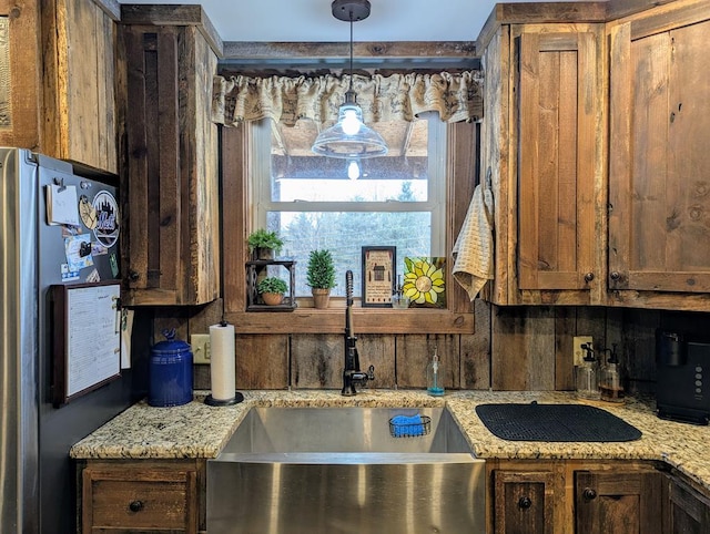 kitchen with light stone counters, decorative light fixtures, decorative backsplash, freestanding refrigerator, and a sink