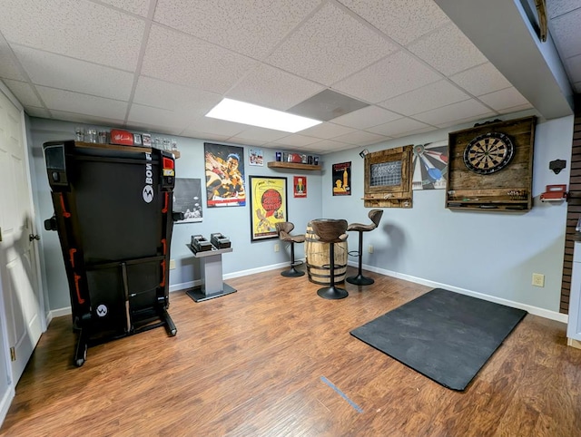 workout area featuring wood finished floors, a paneled ceiling, and baseboards