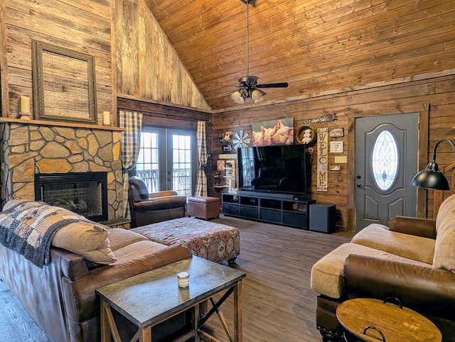 living room featuring wooden walls, wood finished floors, a wealth of natural light, and a stone fireplace