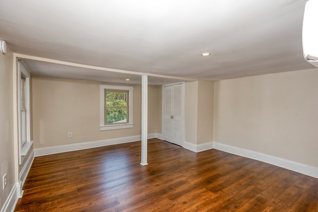 below grade area featuring dark wood-type flooring, an AC wall unit, recessed lighting, and baseboards