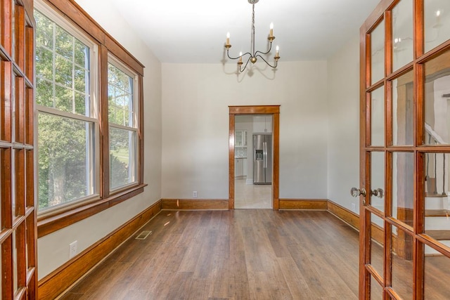 unfurnished dining area featuring visible vents, a chandelier, dark wood finished floors, french doors, and plenty of natural light