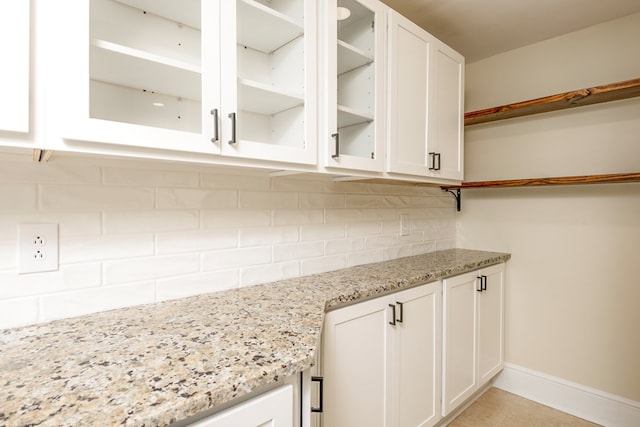 kitchen featuring light stone countertops, open shelves, white cabinets, glass insert cabinets, and tasteful backsplash