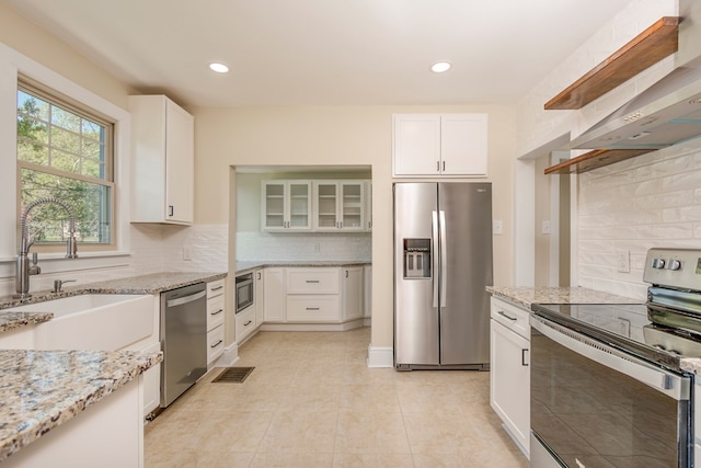 kitchen featuring light stone counters, visible vents, a sink, appliances with stainless steel finishes, and wall chimney range hood