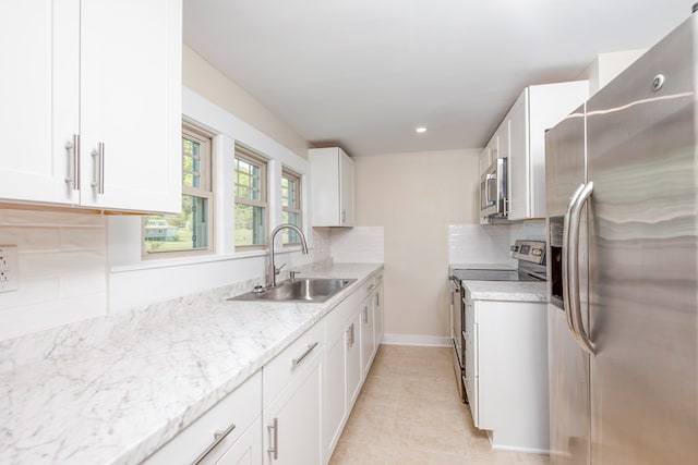 kitchen featuring light tile patterned floors, a sink, decorative backsplash, white cabinets, and appliances with stainless steel finishes