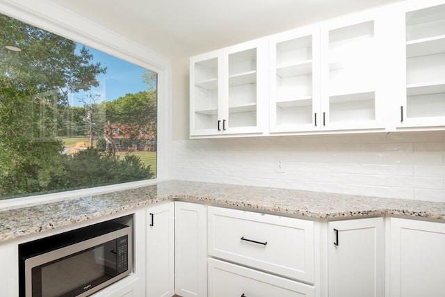 kitchen with light stone counters, glass insert cabinets, white cabinetry, stainless steel microwave, and tasteful backsplash