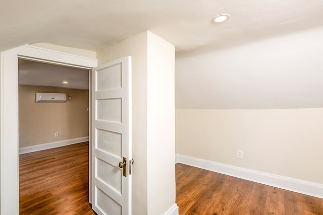 additional living space featuring baseboards, an AC wall unit, dark wood-style floors, and vaulted ceiling