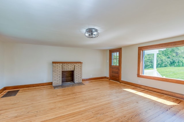 unfurnished living room featuring visible vents, baseboards, a brick fireplace, and wood finished floors