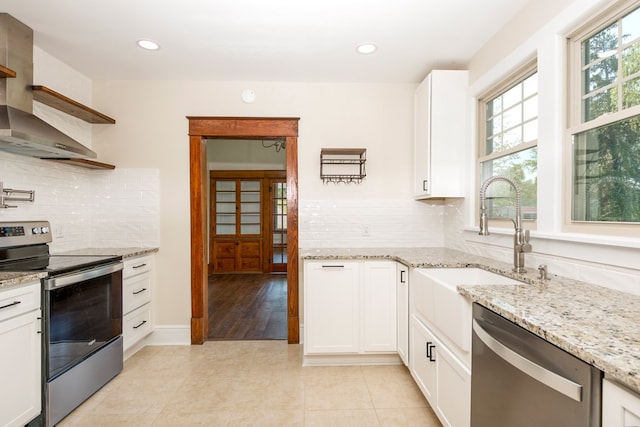 kitchen featuring light tile patterned floors, white cabinetry, appliances with stainless steel finishes, and wall chimney range hood