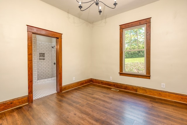 unfurnished room with visible vents, baseboards, an inviting chandelier, and wood finished floors