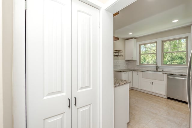 kitchen with tasteful backsplash, light stone countertops, stainless steel dishwasher, white cabinets, and a sink