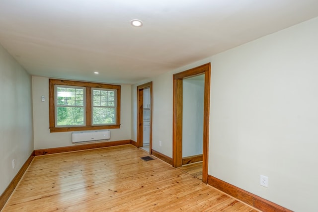 empty room featuring visible vents, an AC wall unit, recessed lighting, light wood finished floors, and baseboards