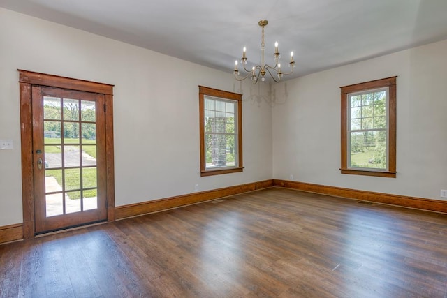 spare room featuring baseboards, wood finished floors, and a chandelier