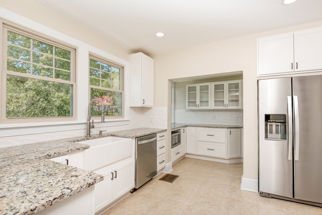 kitchen featuring backsplash, light stone countertops, white cabinets, stainless steel appliances, and a sink