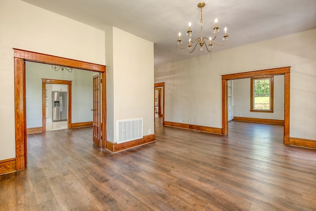 empty room featuring visible vents, baseboards, an inviting chandelier, and dark wood-style flooring