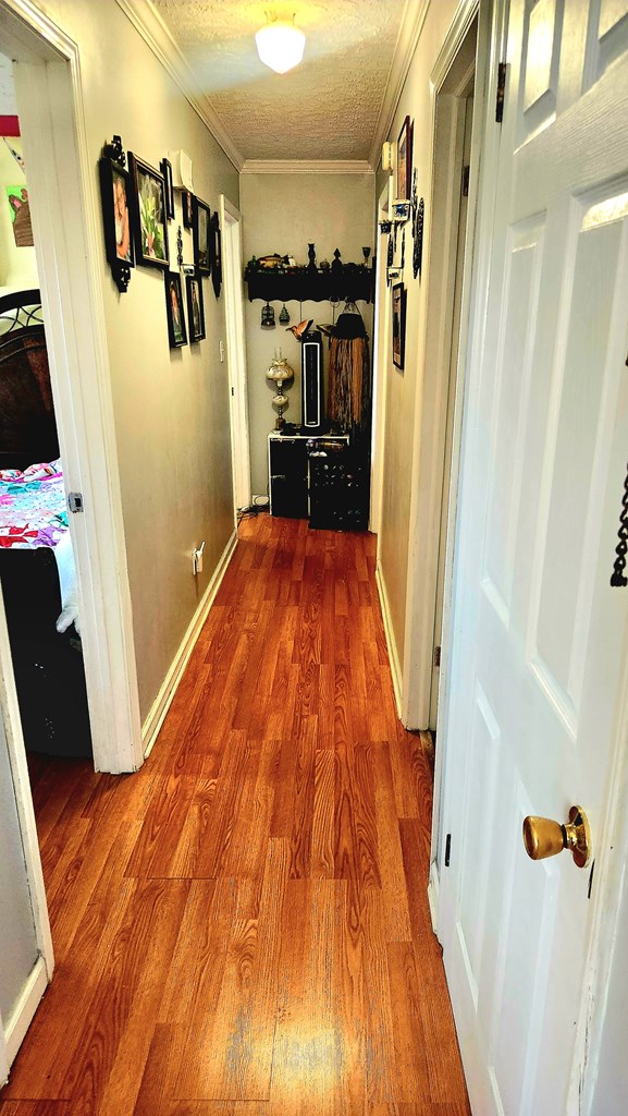 corridor with baseboards, ornamental molding, and wood finished floors