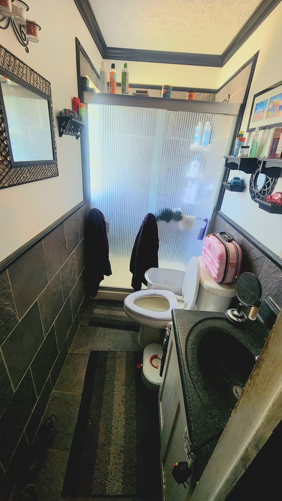 bathroom featuring a textured ceiling, a stall shower, toilet, vanity, and ornamental molding