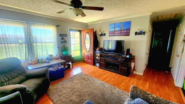 living area featuring wood finished floors, ornamental molding, baseboards, a textured ceiling, and ceiling fan