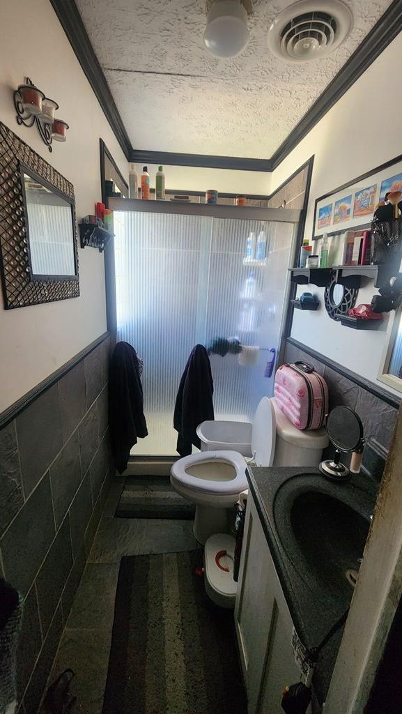 full bathroom featuring a textured ceiling, a shower stall, ornamental molding, and toilet