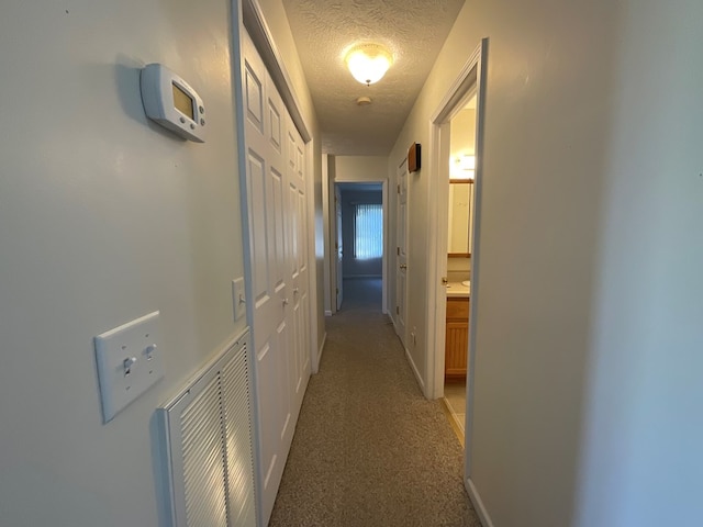 corridor with visible vents, a textured ceiling, and light colored carpet